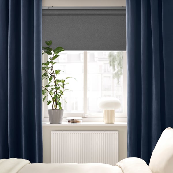 Des rideaux SANELA bleu foncé encadrent une fenêtre avec une plante et une lampe sur le rebord, sous un radiateur blanc.