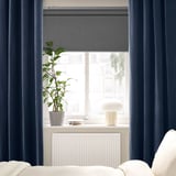 Des rideaux SANELA bleu foncé encadrent une fenêtre avec une plante et une lampe sur le rebord, sous un radiateur blanc.