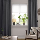 Chambre moderne avec rideaux gris foncé, plante, lampe, chaise à motifs.