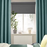 Chambre moderne avec rideaux en velours bleu foncé, plante, lampe et radiateur sur le rebord de la fenêtre, lit en dessous.