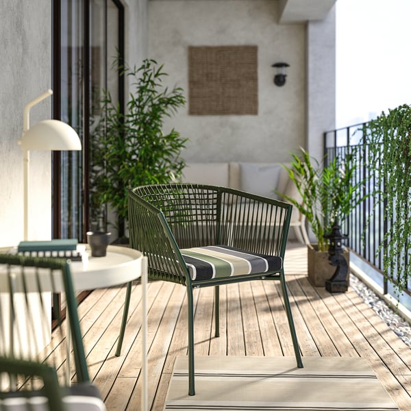 Configuration de balcon moderne avec chaise en osier vert SEGERÖN, coussin rayé, petite table, plantes et décoration murale. Chaise légèrement plus grande que la table.