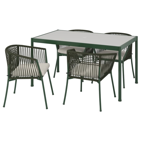 Ensemble de salle à manger d’extérieur vert avec table en verre, 4 chaises tissées et coussins beiges, la table a un trou de parasol.