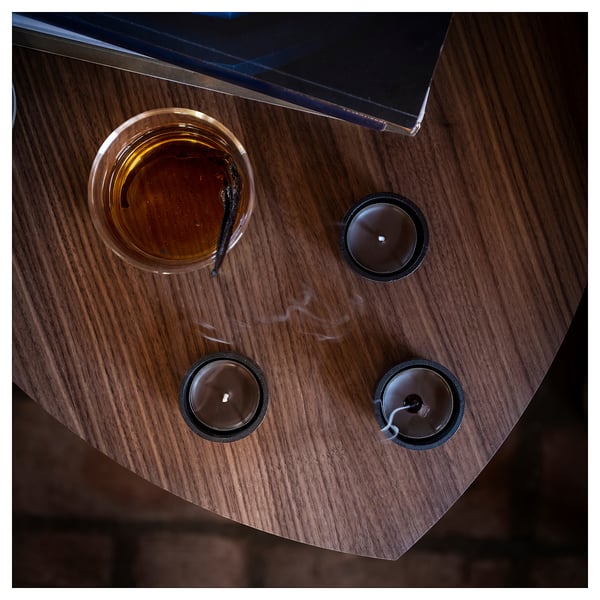 Vue de dessus de trois bougies parfumées allumées, table en bois sombre. Bougies dans des porte-verres, dont une avec bâton, fumée noire.