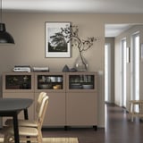 Salle à manger moderne avec buffet SINDVIK, portes vitrées, plats, vase, livres, photo de la nature, chaise en osier.