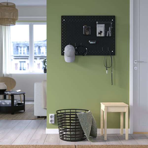 Chambre verte avec panneau perforé SKÅDIS contenant des articles, panier à linge, tabouret, grande fenêtre.