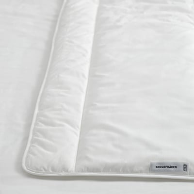 Couette blanche sur le lit, tissu lisse visible, étiquette avec texte indiquant la marque et les matériaux.