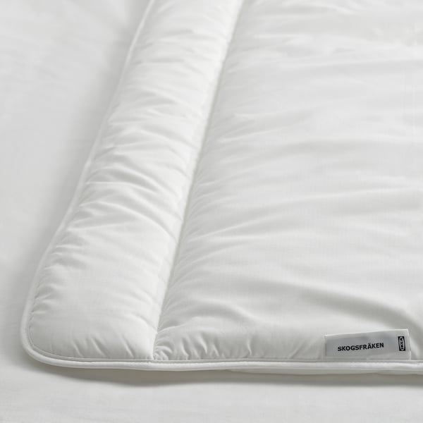 Couette blanche avec un motif doux et matelassé, des bords soigneusement rangés et l’étiquette de la marque ikea SKOGSFRÄKEN visible.