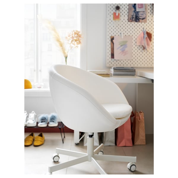 Chaise de bureau blanche moderne avec roues et rembourrage près d’un bureau encombré.