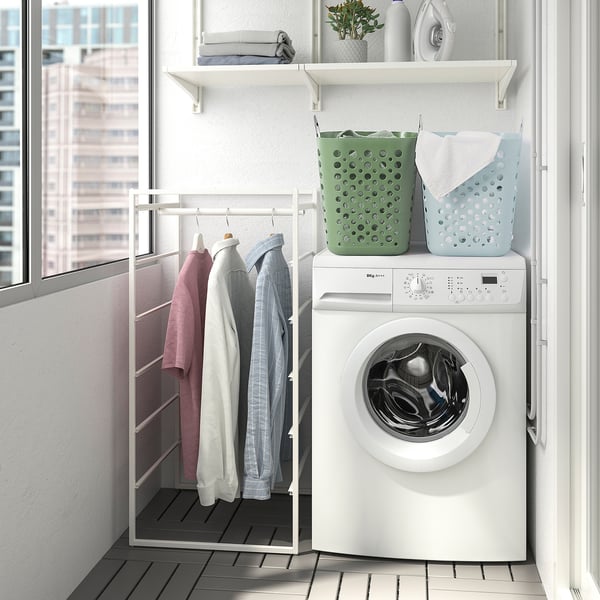 Buanderie moderne avec machine à laver, chemises sur support et paniers à linge colorés.