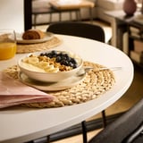 Yogourt, granola, myrtilles dans un bol sur napperon, jus d’orange, serviette de table.