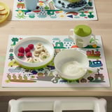 Mise en place de la table pour enfants avec napperon coloré, assiette et bol. L’assiette a des côtés incurvés vers l’intérieur pour un ramassage facile.
