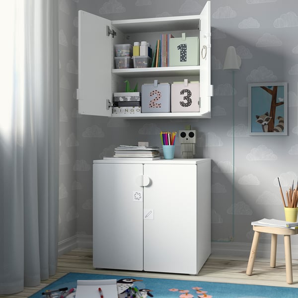 Petite armoire de rangement grise pour enfants avec deux portes et étagères ouvertes au-dessus. Contient des bacs de rangement colorés et des fournitures.