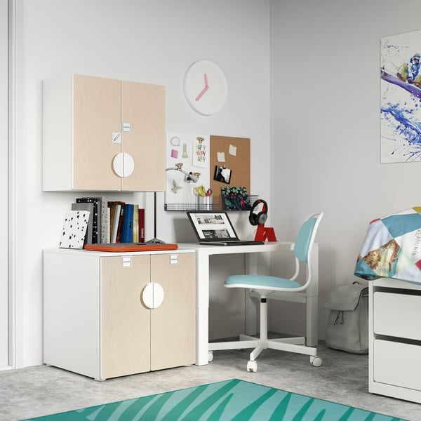 Une chambre d’enfant avec des rangements en bois blanc et clair SMÅSTAD, une chaise bleue, un bureau et des décorations colorées.