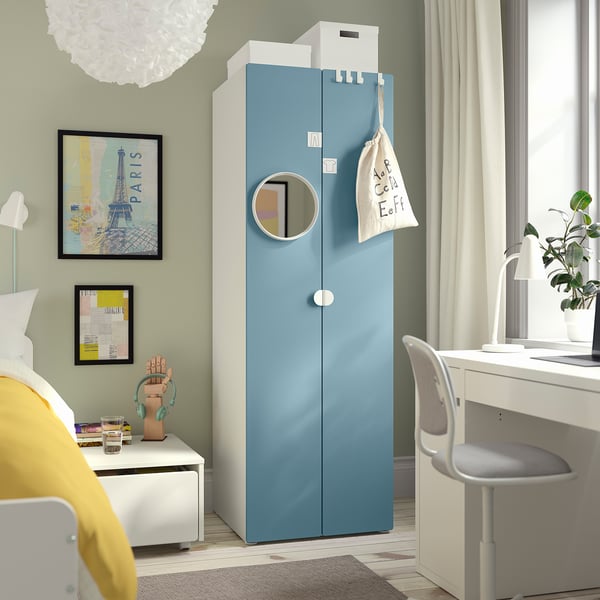 L’armoire bleue SMÅSTAD s’élève près d’un bureau et d’une chaise blancs. La chambre comprend un lit avec des oreillers jaunes, des œuvres d’art, un tapis.