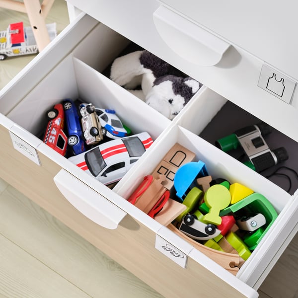 Coffre à jouets blanc ouvert avec des compartiments remplis de jouets colorés et d’animaux en peluche.