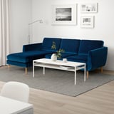 Salon moderne avec grand canapé SMEDSTORP en velours bleu, table basse blanche, tapis gris et art mural. Lumineux et accueillant.