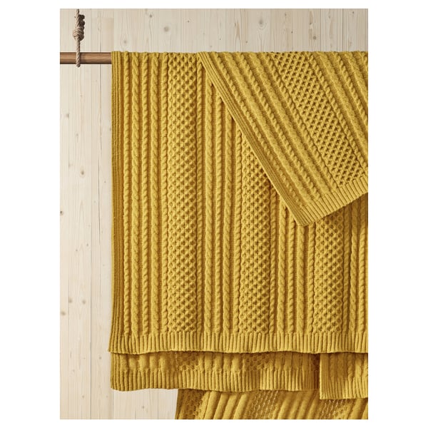 Plaid SÖRBYSKOGEN jaune moutarde exposé sur une poutre en bois ; Motif en tricot texturé, drapé soigneusement.