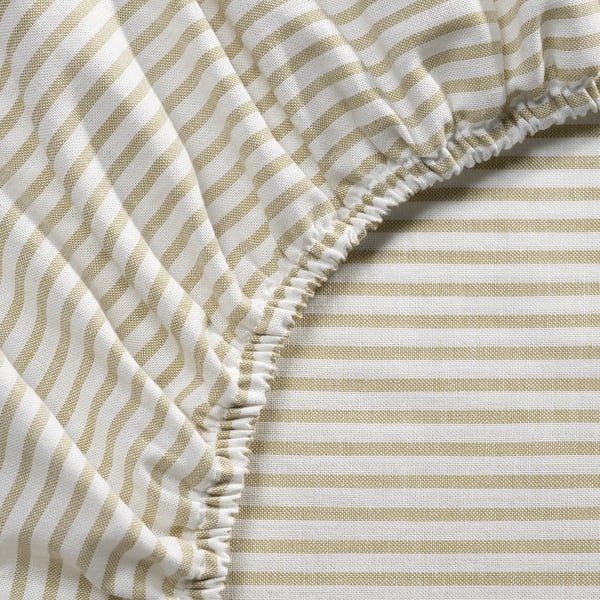 Gros plan du drap de lit rayé beige et blanc avec bord élastique, mettant en valeur les coutures détaillées.