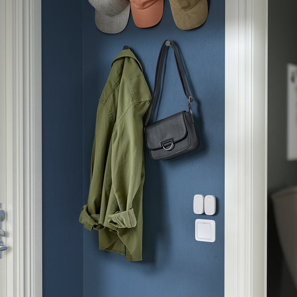 Un mur bleu, monté avec des vestes, des chapeaux et un sac à main. Ci-dessous, un bouton pour la domotique intelligente.