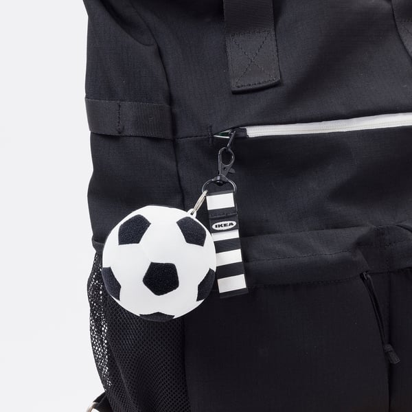 Sac à dos noir avec breloque latérale en forme de ballon de football, marquage CE, étiquette IKEA visible.