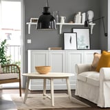 Salon moderne avec tapis léger, table basse blanche, fauteuil beige, suspension noire et tapis aux tons naturels.