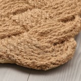 Paillasson fait à la main avec un tissage épais et naturel de la fibre de coco, exposé sur un plancher en bois, mettant en valeur un savoir-faire robuste.