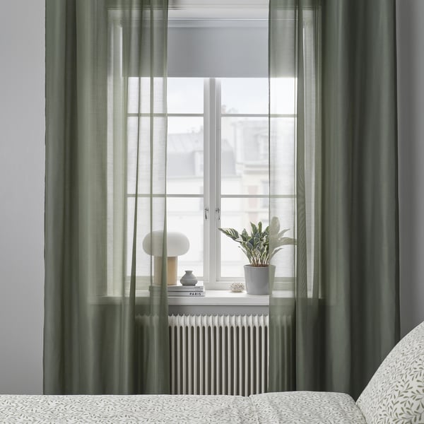 Fenêtre de la chambre avec rideaux transparents STENFRÖ en vert, œillets, radiateur blanc en dessous, lumière diffuse.