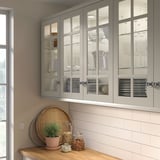 Les armoires de cuisine modernes beiges STENSUND avec portes en verre mettent en valeur la porcelaine fine. Design mince avec poignées argentées, s’adaptant élégamment au-dessus du comptoir.