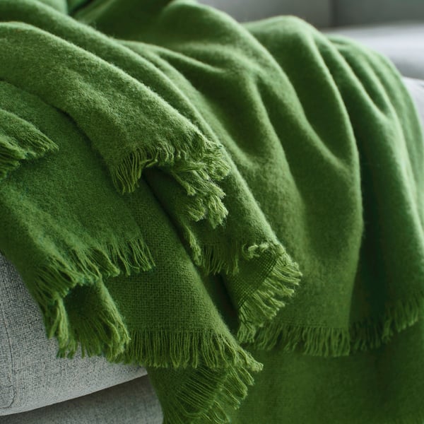 Couverture verte brillante tissée à la main avec frange drapée en douceur, mettant en valeur la douce texture de la laine mérinos.