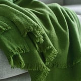 Couverture verte brillante tissée à la main avec frange drapée en douceur, mettant en valeur la douce texture de la laine mérinos.