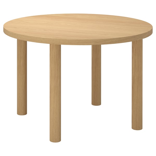 Une table à manger ronde IKEA STOCKHOLM 2025 en brun clair, en placage de chêne. Il a un design minimaliste et robuste avec quatre pieds droits.