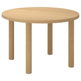 Une table à manger ronde IKEA STOCKHOLM 2025 en brun clair, en placage de chêne. Il a un design minimaliste et robuste avec quatre pieds droits.