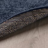 Tapis gris foncé avec poils épais et doux et bord texturé sur parquet clair.