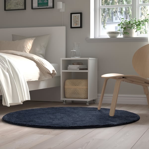 Chambre confortable avec tapis bleu, parquet, lit, table de chevet, plantes, chaise.