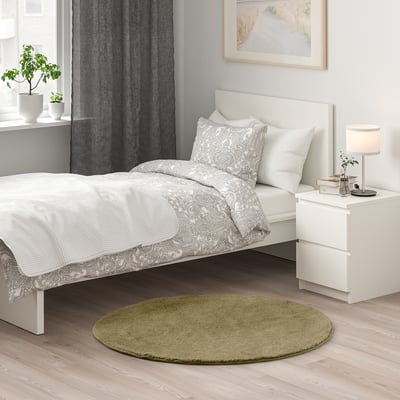 Chambre confortable avec tapis vert STOENSE à côté du lit blanc, ajoutant de la chaleur.