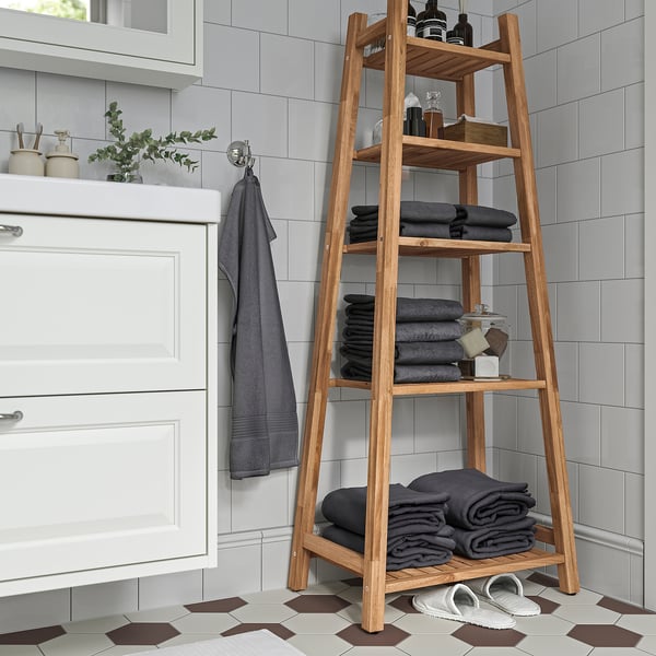 Étagère en bois d’acacia dans la salle de bain avec serviettes et articles de toilette.