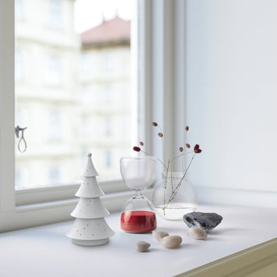 Petite lampe STRÅLA blanche à côté d’une bougie rouge, de vases transparents et de pierres près de la fenêtre.