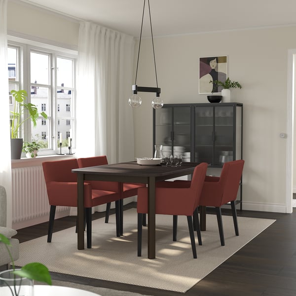 Salle à manger moderne avec table STRANDTORP, chaises rouges et armoire. Peut accueillir jusqu’à 8 personnes. Bois sombre, socle en métal, décor minimaliste.