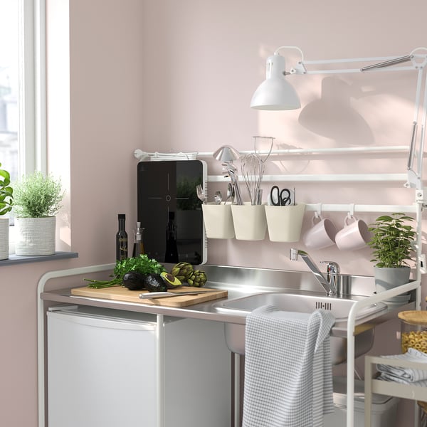Petit organisateur suspendu SUNNERSTA en plastique blanc, tenant les ustensiles de cuisine près d’un évier.