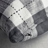 Noir et blanc, une housse de coussin avec un motif à carreaux traditionnel, montrant des coutures apparentes et une fermeture éclair.