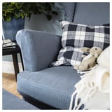 Fauteuil rayé bleu et blanc avec coussin à carreaux et ours en peluche. Configuration confortable du salon.