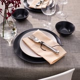 Table avec des assiettes grises, des serviettes beiges, de l’argenterie, des bols, des verres à vin et un vase avec des fleurs rouges.