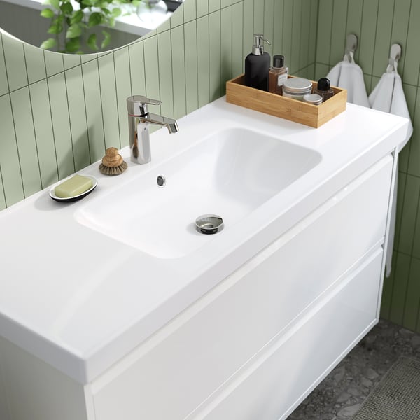 Vanité de salle de bain blanche moderne avec lavabo intégré, robinet argenté et plateau en bois avec articles de toilette sur un mur carrelé vert clair.