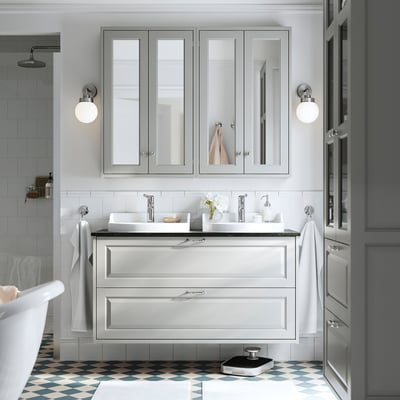 Salle de bain moderne : vanité blanche, grise, baignoire, murs carrelés, sol en damier.