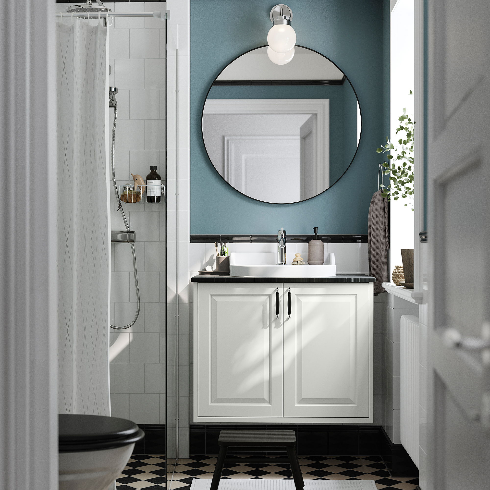 Salle de bains moderne TÄNNFORSEN vanité blanche, miroir rond, carrelage noir et douche en verre. Lavabo et toilettes visibles, avec des murs bleus.