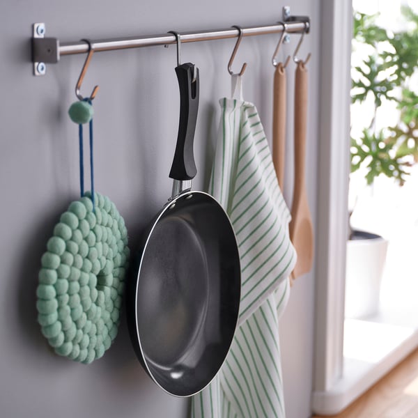 Grille en acier inoxydable avec objets suspendus : poêle, gant texturé, serviette rayée.