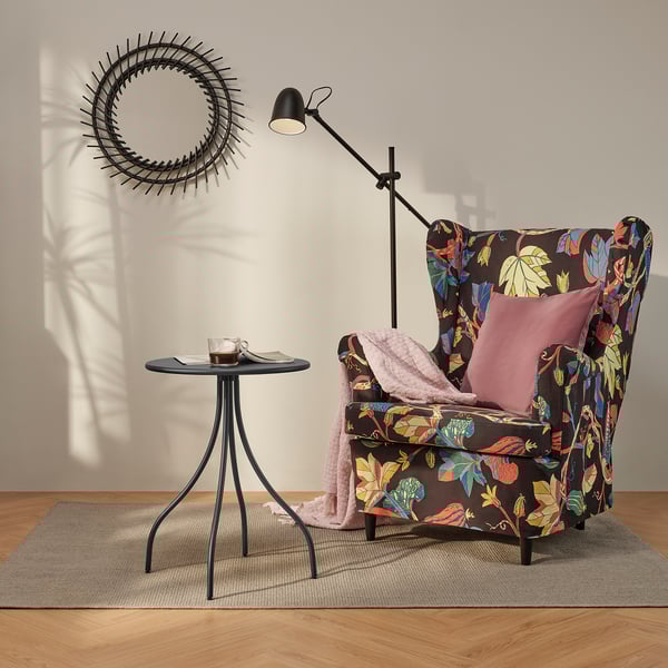 Fauteuil floral dans un coin confortable avec table d’appoint, couverture, oreiller, lampe, tapis, décoration.