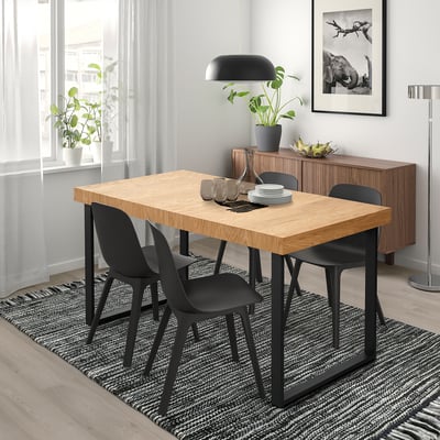 Ensemble de salle à manger moderne avec table TARSELE, 4 chaises noires, grande suspension, plantes, photo d’éléphant et tapis léger.