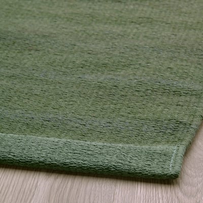 Cette image montre le TIDTABELL, un tapis rectangulaire vert avec une surface en laine et un support en coton. Son tissage plat et un subtil motif mélangé.