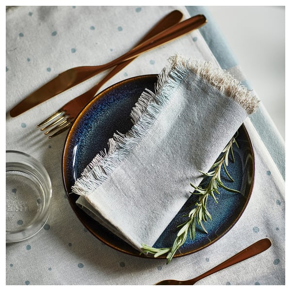 Table avec assiette mouchetée bleue, serviette blanche pliée à franges et couverts en laiton bien rangés.